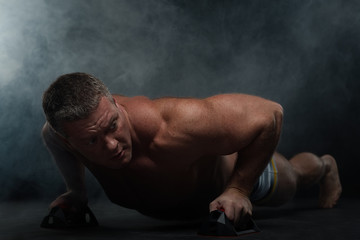 Obraz premium muscular man does pushups in the smoke on a black background