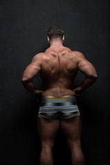 Fototapeta na wymiar powerful muscular athlete shows off his back near a black grunge wall