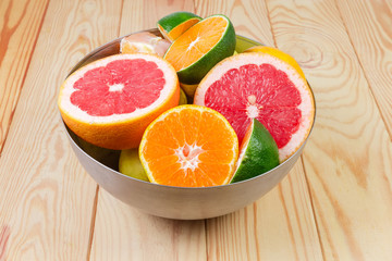 Different partly cut citrus in metal bowl on wooden table