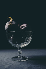 Pile of fresh ripe plums in glass cup at the table photographed in low light