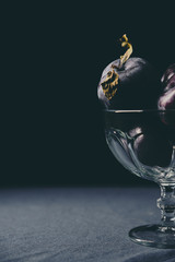 Pile of fresh ripe plums in glass cup at the table photographed in low light