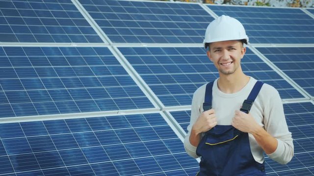 Portrait of a worker in a helmet, looking at the camera, stands against the background of a row of solar panels. alternative energy