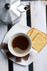 Coffee in a geyser coffee maker cookie and candy on a saucer stand on a wooden box.