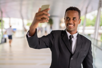 Happy African businessman taking selfie using mobile phone outdoors