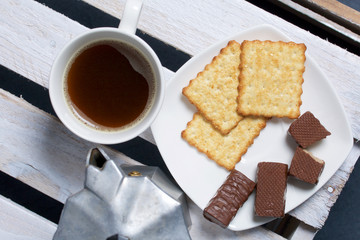Coffee in a geyser coffee maker cookie and candy on a saucer stand on a wooden box.