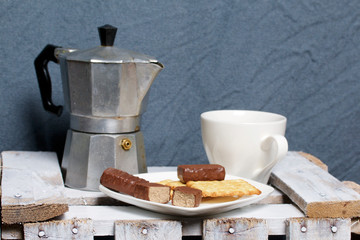 Coffee in a geyser coffee maker cookie and candy on a saucer stand on a wooden box.
