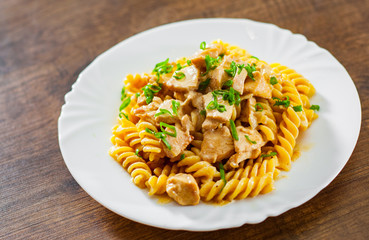 Sliced fried chicken fillet in a creamy sauce with fusilli pasta in white plate on wooden table