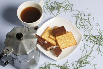 Coffee in a geyser coffee maker cookie and candy on a saucer stand on a wooden box. On a white background sprinkled with fir needles.