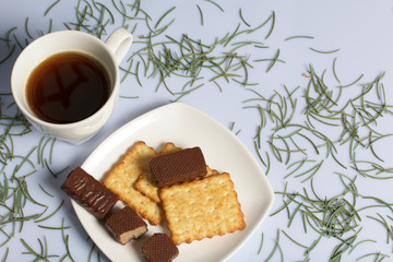 Coffee, cookie and candy on a saucer stand on a wooden box. On a white background sprinkled with fir needles.