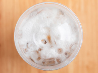 Close up and top view. A plastic cup of ice coffee is placed on wooden table.