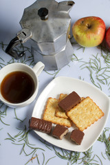 Coffee, cookie, apples and candy on a saucer stand on a wooden box. On a white background sprinkled with fir needles.