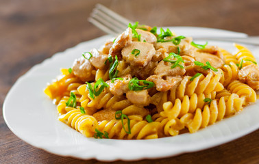Sliced fried chicken fillet in a creamy sauce with fusilli pasta in white plate on wooden table