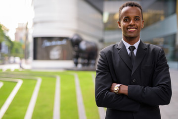 Fototapeta premium Successful young African businessman smiling outdoors with arms crossed