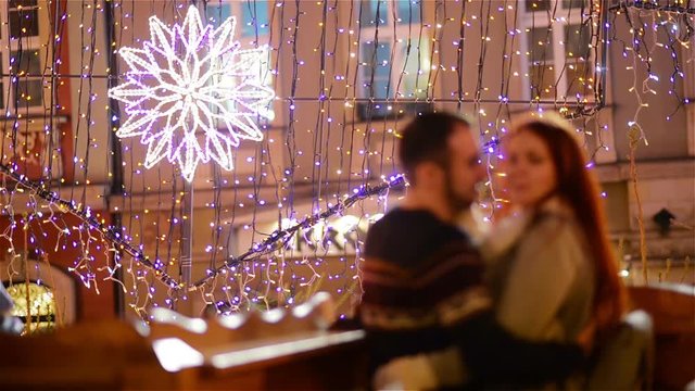 Romantic Couple with the Caucasian Appearance Kissing and Cuddling. Lights and Fireworks are On Background. Young Couple Canoodling with Yourself This Romantic Night.