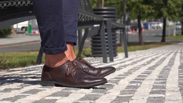 A businessman sits on a bench in an urban area - closeup on the shoes