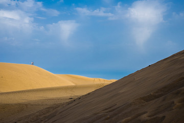 Couple of tourist standing on the hill of a dune in the yellow sandy desert. contrast of colors with blue celar sky. light and shadow. amazing natural outdoors background