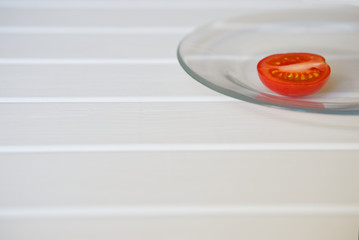 A half of fresh tomato lies on a transparent plate on a white background