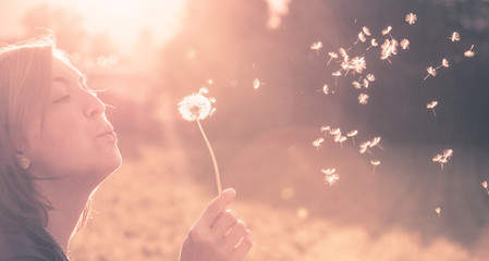 Junges Mädchen bläst Samen einer Pusteblume, Sonnenuntergang im Herbst mit Textfreiraum