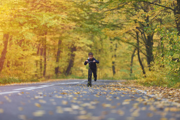 Cute boy riding scooter, outdoor in autumn environment on sunset warm light
