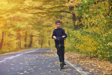 Cute boy riding scooter, outdoor in autumn environment on sunset warm light