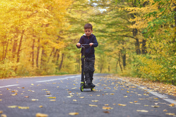 Cute boy riding scooter, outdoor in autumn environment on sunset warm light