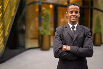 Happy young African businessman wearing suit outdoors with arms crossed