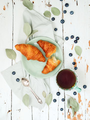 Top view of fresh croissants served with ripe blueberries and apricot jam  with tea on green plate over shabby background © PINKASEVICH