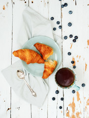 Top view of fresh croissants served with ripe blueberries and apricot jam  with tea on green plate over shabby background © PINKASEVICH