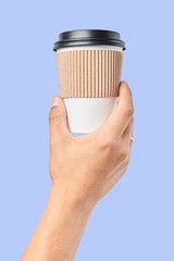 Mockup of men's hand holding white paper mid size cup with black cover isolated on blue background