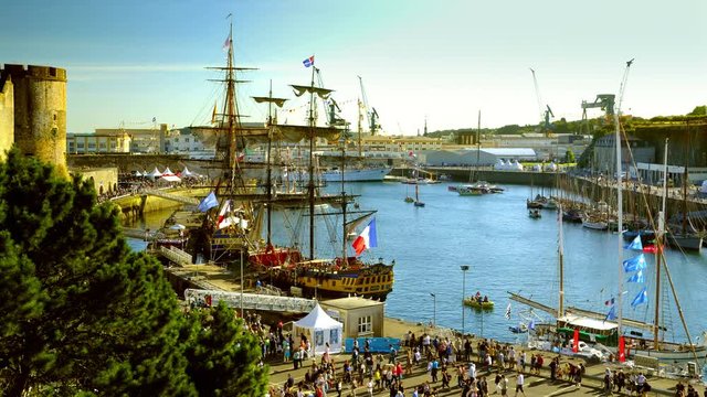 Brest, France - July 14, 2016: Old ships in timelapse: Etoile du Roy, Hermione, Cuauhtemoc in the harbor of Brest. Crowd, french flags and small boats moving fast. Colorful scenery at Golden hour.