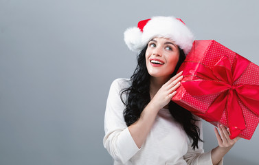 Young woman with santa hat holding a gift box on a gray background