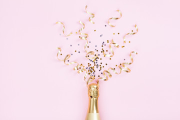 Champagne bottle with confetti stars and party streamers on pink background. Christmas, birthday or wedding concept. Flat lay style.