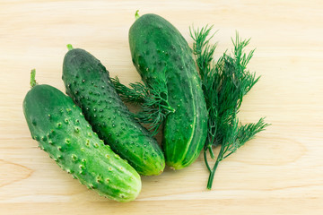 fresh cucumber three vegetables with a sprig of dill on a light beige wooden background close-up of a light snack diet