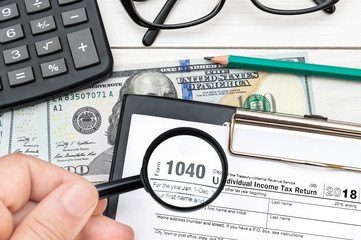 Hand holding magnifying glass over tax form at office workplace.