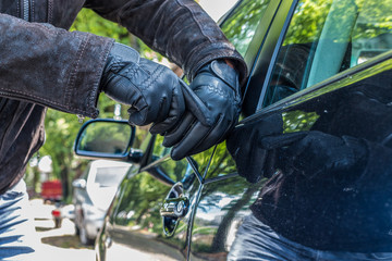 A person with is trying to break the lock of a car with a screwdriver