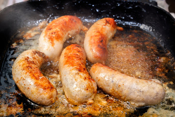 Sausages are fried in boiling oil in a hot frying pan. Close-up