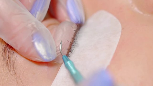 beautician is making procedure of lamination of eyelashes, fixing patch on eyelid and stroking lashes, close-up