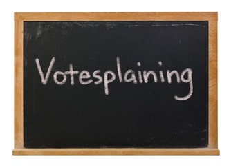 Votesplaining written in white chalk on a black chalkboard isolated on white