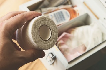 Hand grabbing a bandage roll from a vintage first aid box. Medical supplies concept image. 