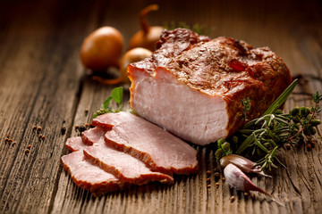 Smoked meats, sliced smoked pork loin on a wooden  table with addition of fresh  herbs and aromatic spices.  Traditional smoked meat smoked in apple  and beech  wood, Natural product from organic farm