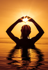 Silhouette of beautiful girls make a heart with her hands in the infinity pool.