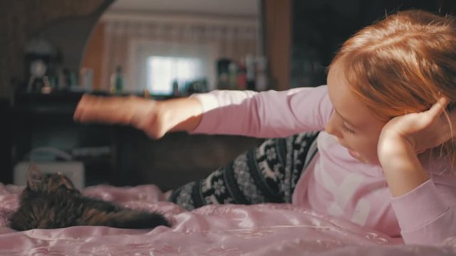 Little cute girl playing with kitten on bed at home.