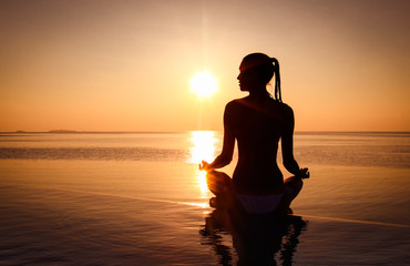 Woman has meditation and Yoga at infinity pool during sunset.