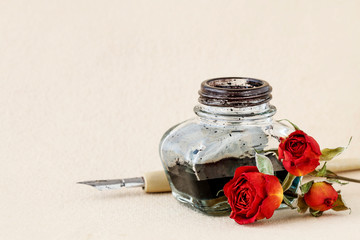 Inkwell, pen and dried roses on vintage paper background