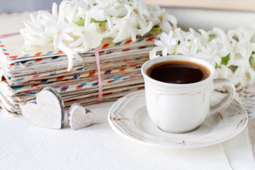 Cup of coffee, stack of old letters, hyacinth flower and white feathers.