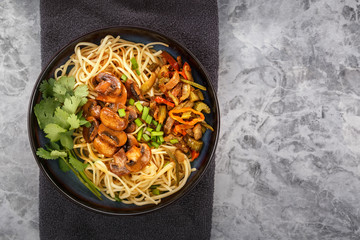 Traditional Chinese noodles noodles with fried meat and salad in a porcelain plate on a gray table. Copy space. Top view