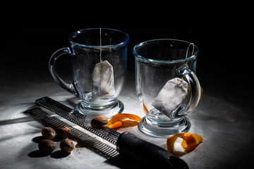 Two Cups of Hot Tea With Orange Peels, Nutmeg and Grater On Marble With Dark Background.
