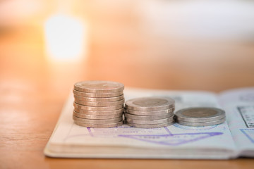 Business, Saving and Travel Concept. Close up of Stack of coins on passport with immigration stamps on wooden table.