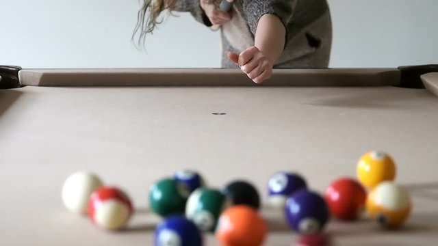 Slow motion of young woman aiming, pointing pool billiard cue against white ball, taking break shot at home, house, apartment living, game room inside, indoors, indoor