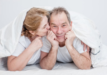 Senior woman kissing husband under blanket